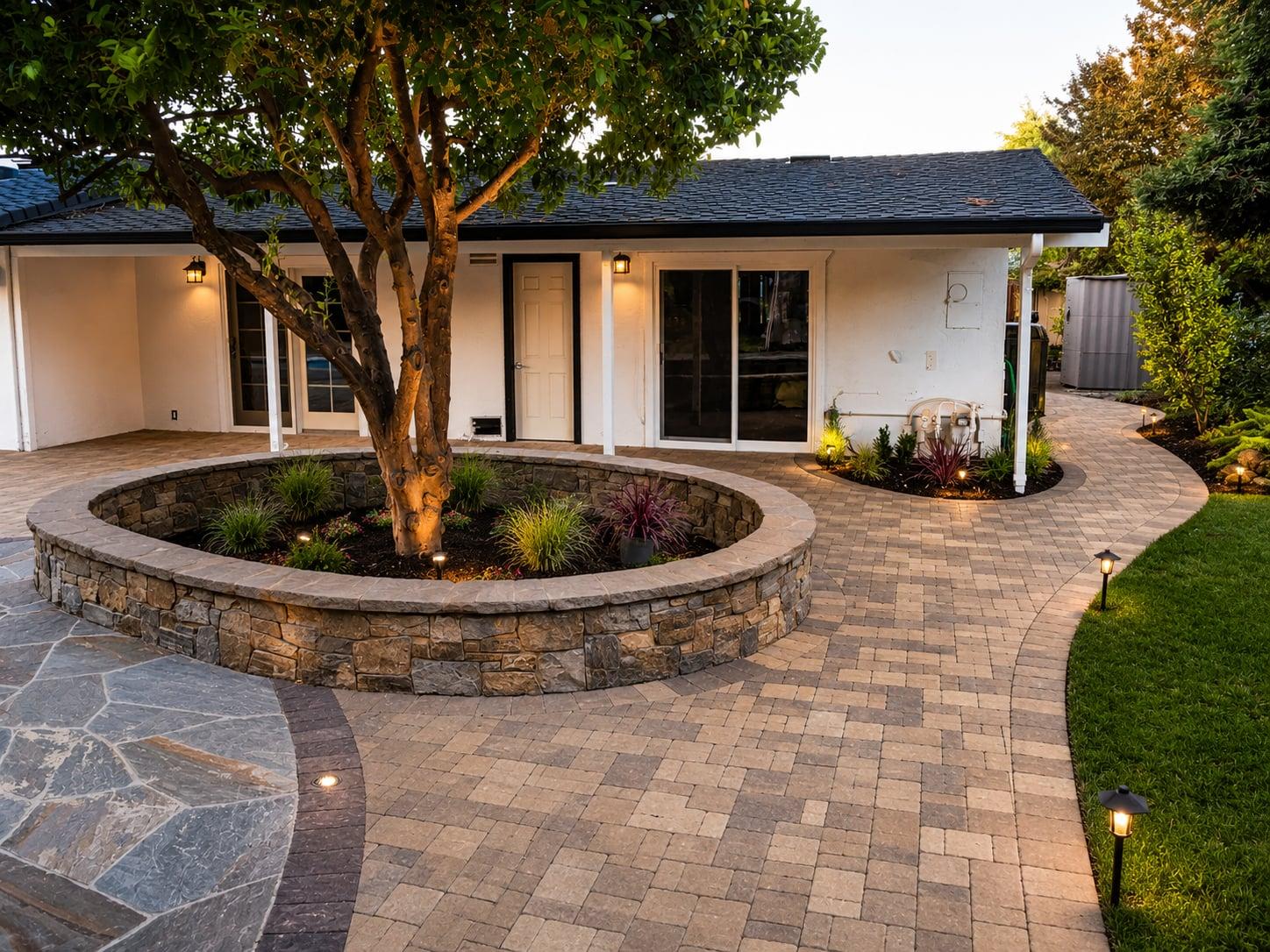 Custom paver patio with circular stone-walled tree planter and integrated landscape lighting at an Orinda, CA home